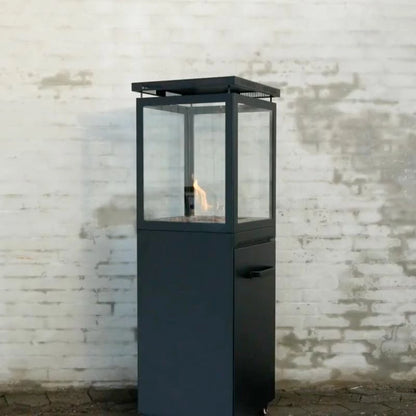Black outdoor fire pit with glass cover against a textured white brick wall.
