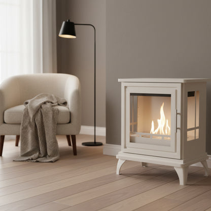Oyster white freestanding fireplace with glass door in a dark cream room with a standard lamp, a chair and thrwo.