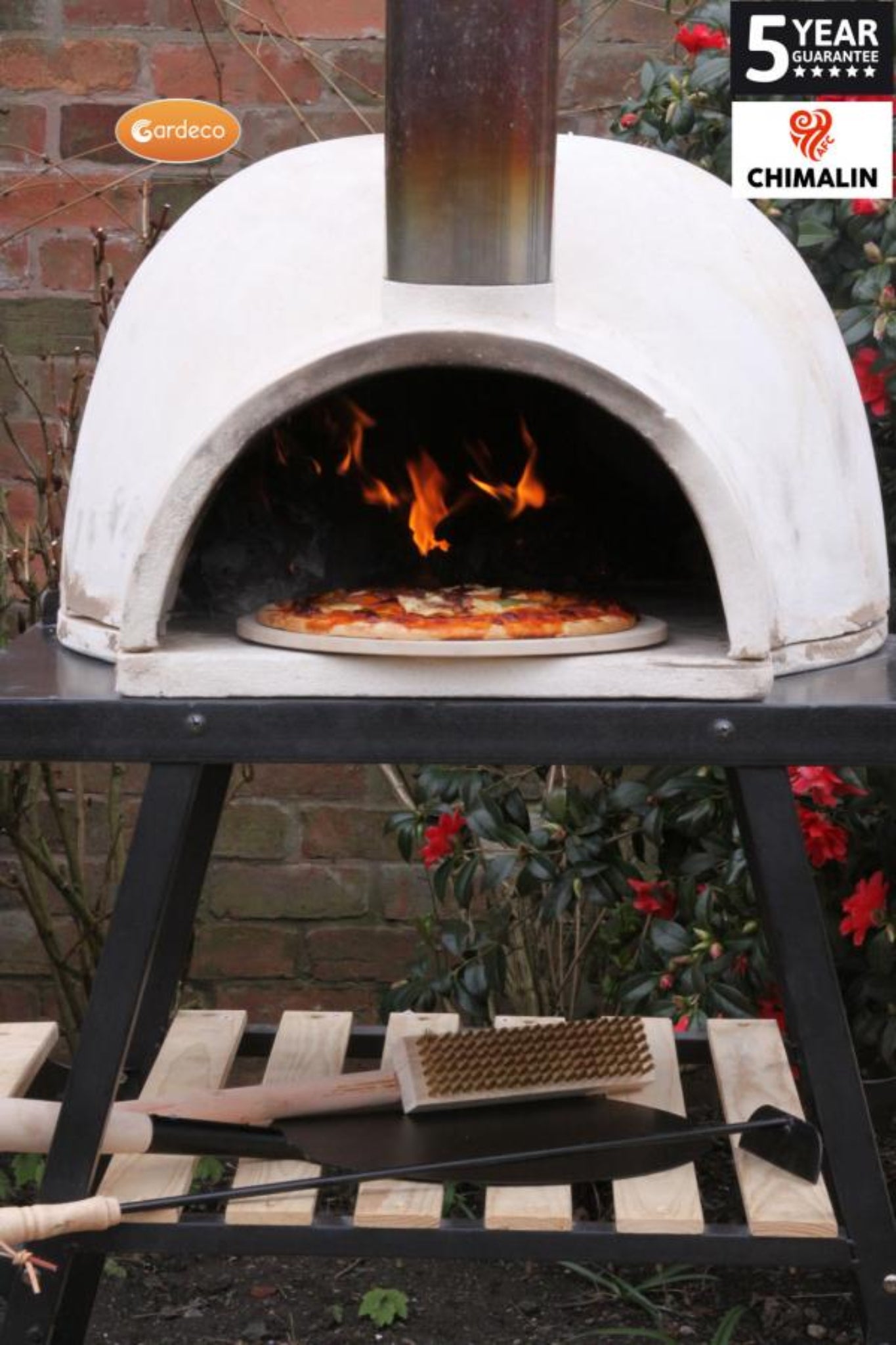 Outdoor pizza oven with a pizza being cooked, surrounded by garden elements.