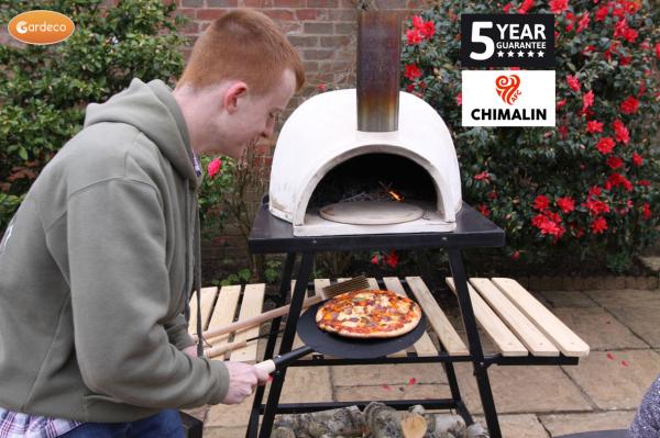 Person cooking pizza in a portable outdoor oven with Gardeco branding and Chimalin guarantee displayed.
