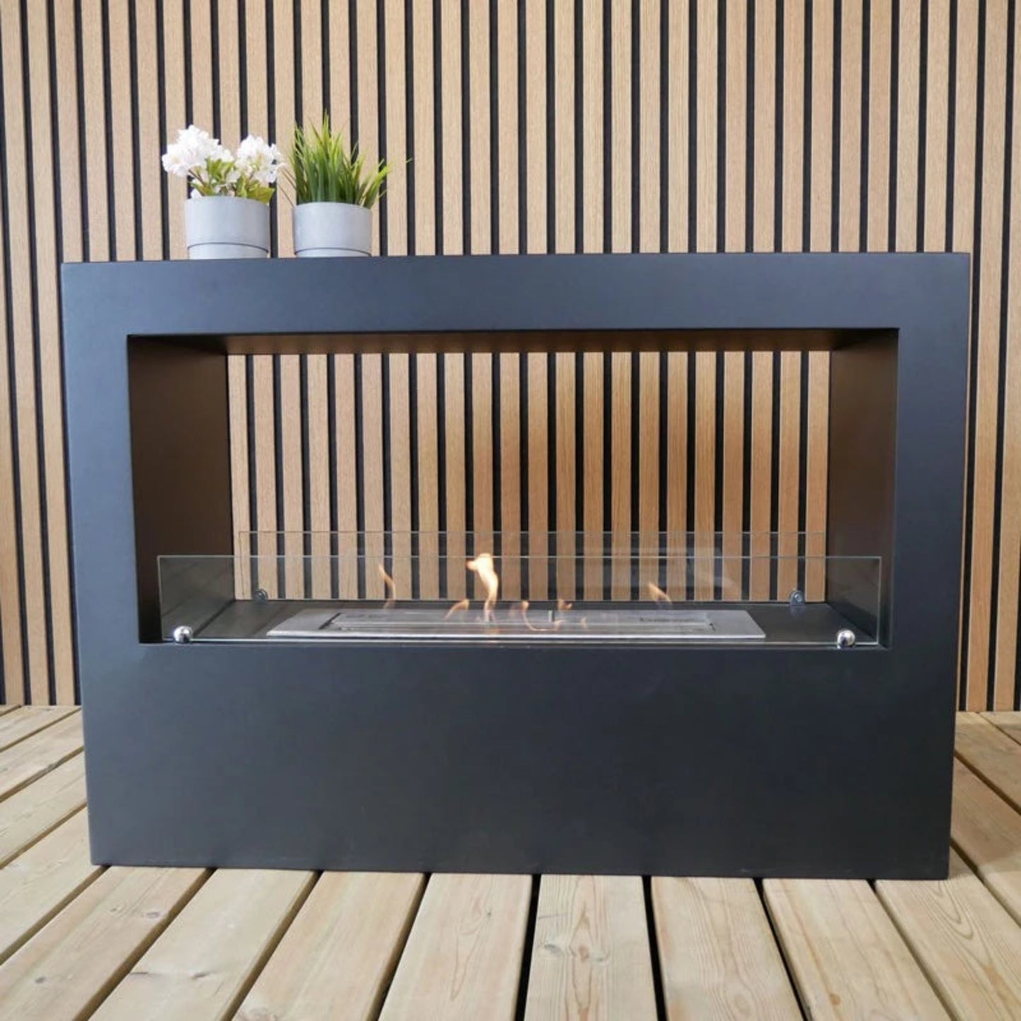 Modern outdoor ethanol fireplace on a wooden deck with plants on the mantel.